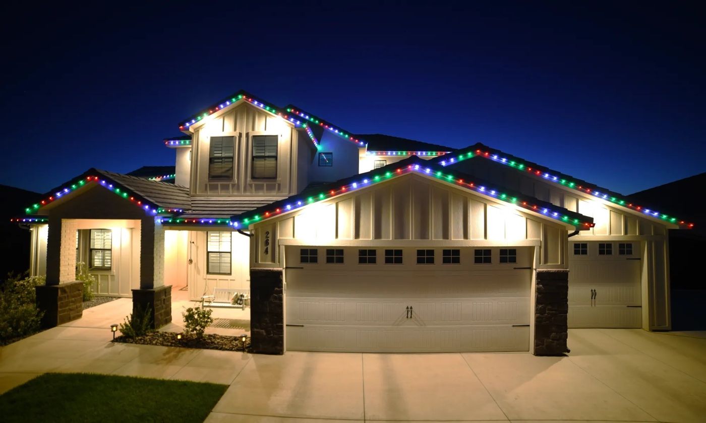 A two-story home lit with festive multicolor holiday lights at night