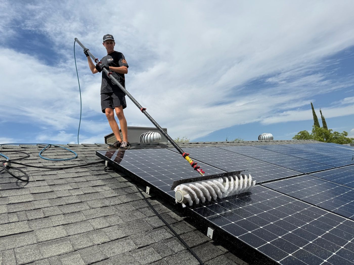 Lumon technician cleaning rooftop solar panels with a water-fed pole brush