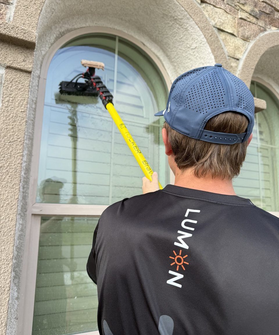 Lumon technician in branded shirt cleaning a window with a water-fed pole